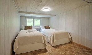 Ein Zimmer mit zwei Betten, Holzboden und einem Fenster.