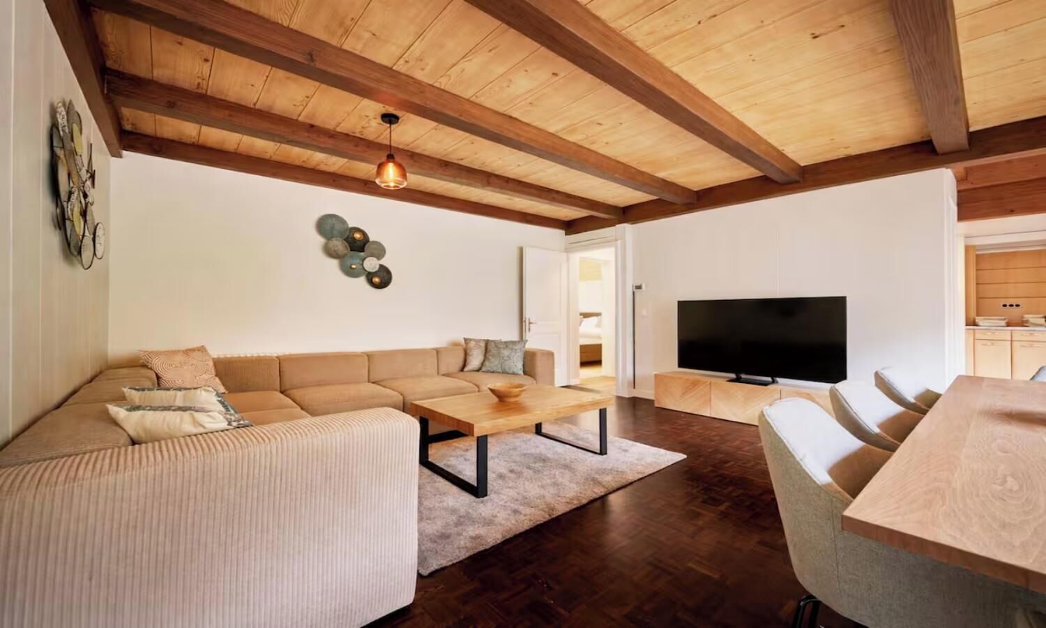 Ein modernes Wohnzimmer mit einer Eckcouch, einem Couchtisch, einem Fernseher und einem Essbereich mit Tisch und Stühlen.