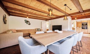Ein modernes Interieur mit Holzboden, einem Esstisch mit Stühlen, einer Couch und einem Fernseher.
