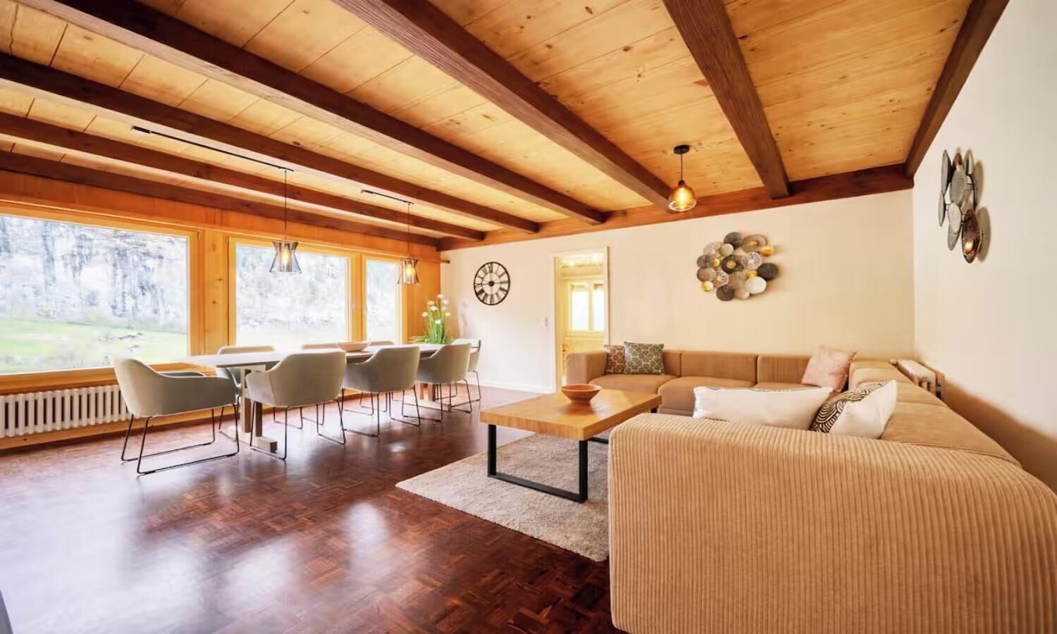 A spacious living area with a wooden ceiling, a dining table with chairs, a sofa, and a decorative wall piece.