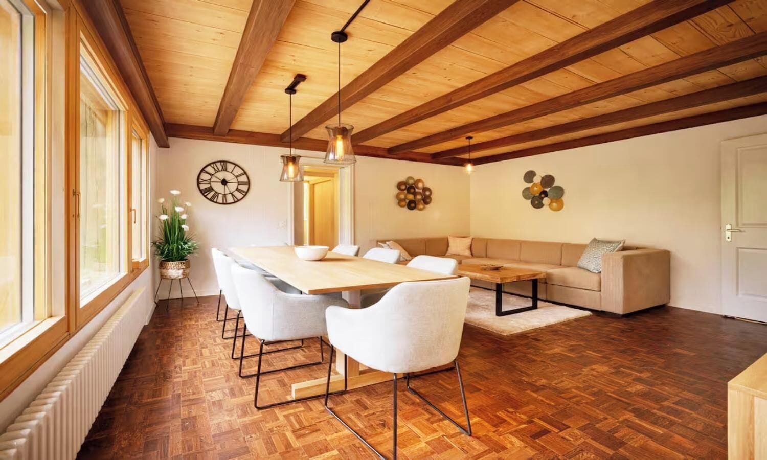A dining area with a wooden table and chairs, a sofa, and a decorative wall clock.