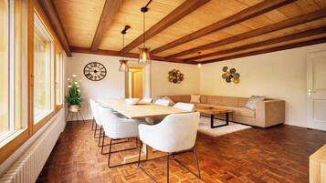 A dining area with a wooden table and chairs, a sofa, and a decorative wall clock.