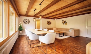 A dining area with a wooden table and chairs, a sofa, and a decorative wall clock. - MODERN CHALET RETREAT WITH ICONIC LAUTERBRUNNEN VIEWS (Lauterbrunnen)
