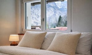 A bedroom with a bed, a nightstand, a lamp, and a window with a mountain view.