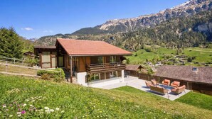 Un chalet moderne avec un toit recouvert de tuiles rouges, un balcon et une vue sur un paysage montagneux.