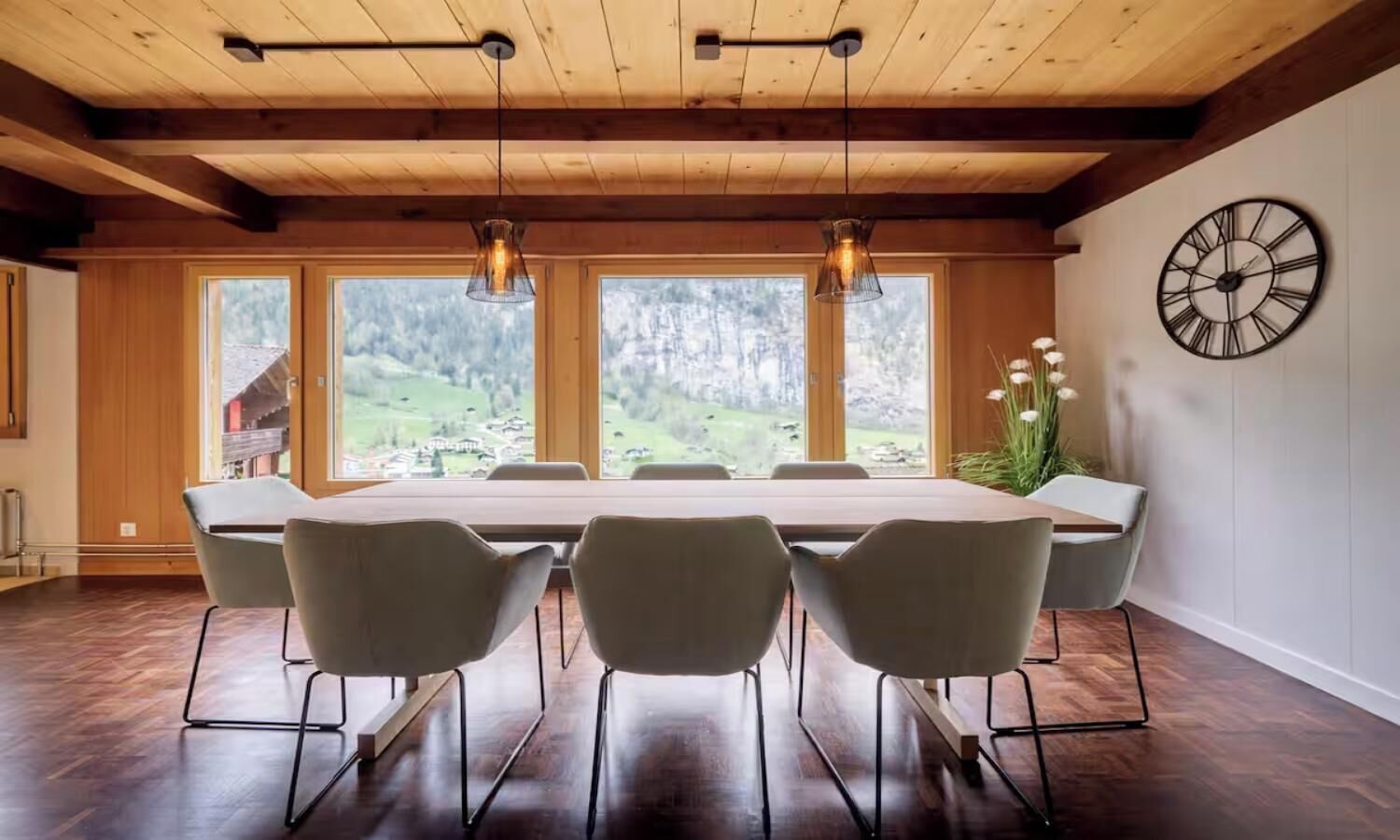 A dining area with a long table, six chairs, and pendant lighting.