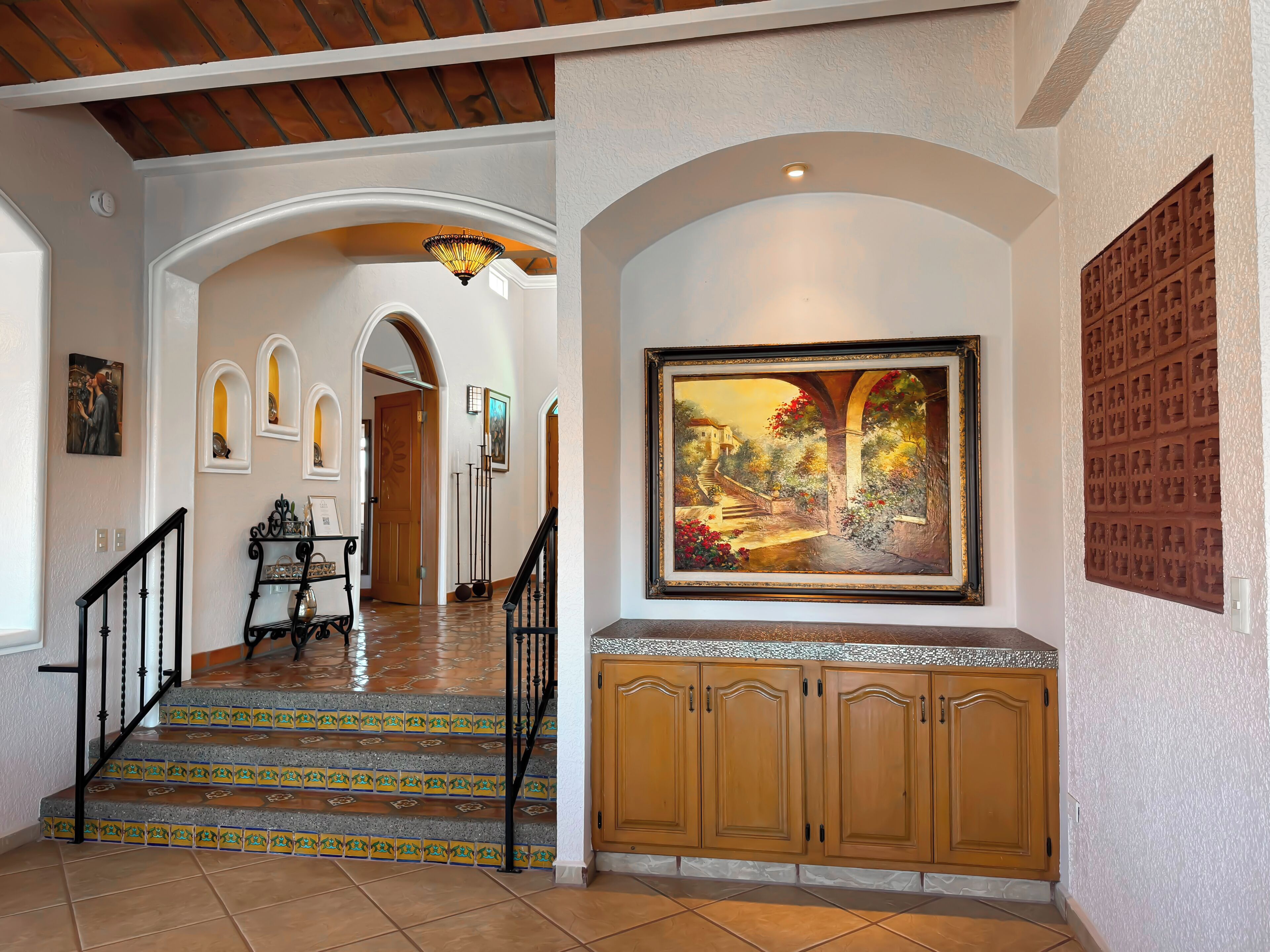 A hallway with a staircase, a painting, and wooden cabinets.