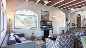 A living room with a flat-screen TV, a sofa, a patterned armchair, a potted plant, and a large window. - Panoramic Sea of Cortez Views at Casa Arco (San Carlos)