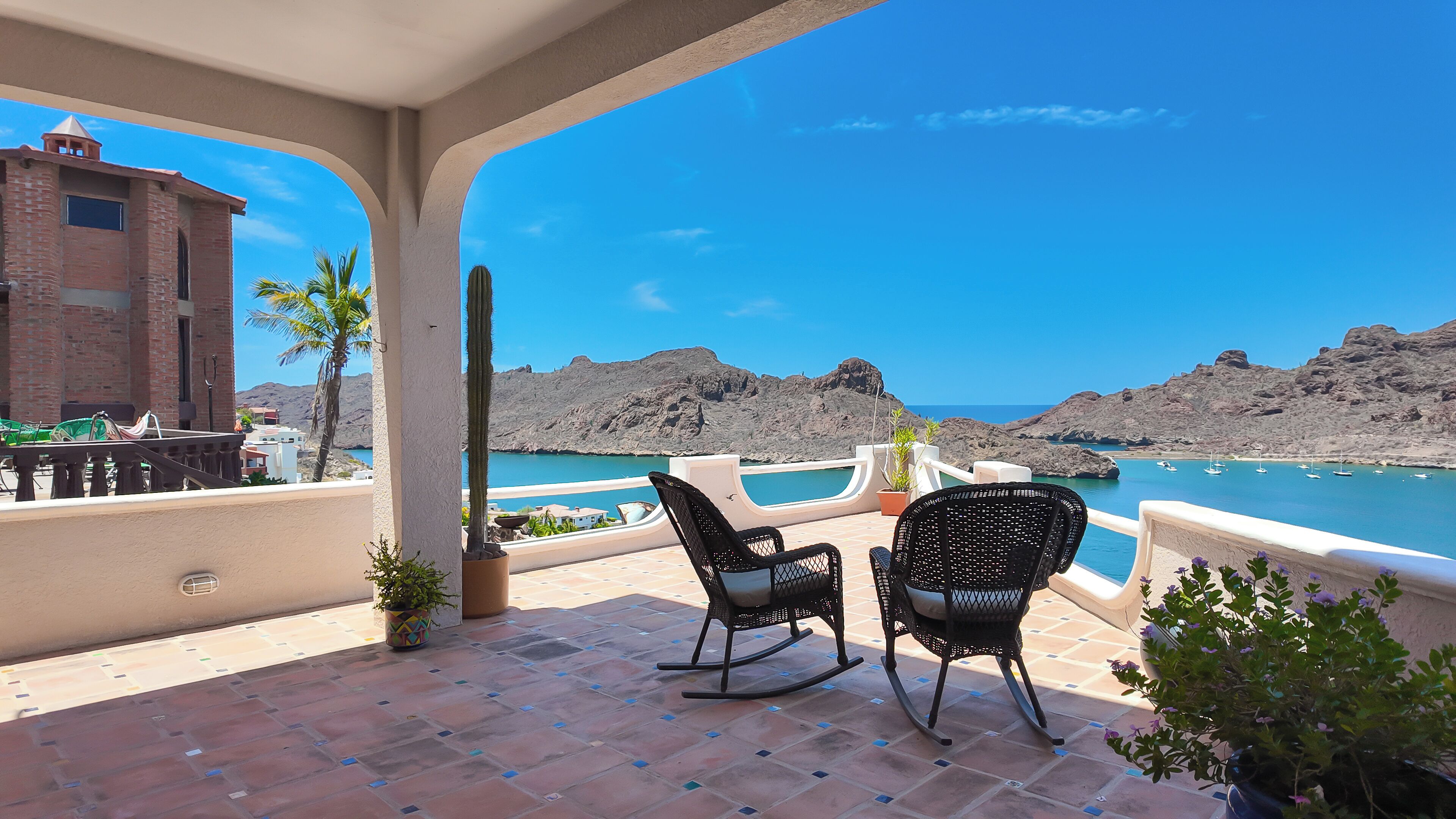 A terrace with two rocking chairs, a view of the sea, and a building with a brick facade.