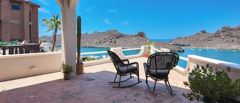 A terrace with two rocking chairs, a view of the sea, and a building with a brick facade.