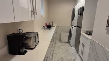 Une cuisine moderne avec des meubles blancs, un sol en marbre, un grille-pain, un lave-linge et un four à micro-ondes.