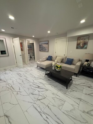 A living room with a marble floor, a beige sofa with blue cushions, and a coffee table with flowers. - Modern 1BR Lake Washington Blvd Suite – Private, lake WA, parks & resturants (Kirkland)