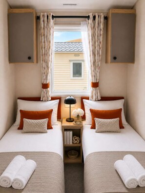 A bedroom with two beds, a nightstand with a lamp, and a window with curtains. - Sandy Toes New 2026 Stylish 2Bed Steps from Beach (Challaborough)