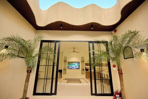 A hotel entrance with a modern design, featuring a large glass door, a ceiling fan, and potted palm plants. - Mediterranean pool villa near the beach (Thành phố Hồ Chí Minh)