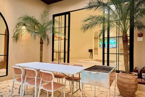 A room with a white table and chairs, a grill, and two large potted plants. - Mediterranean pool villa near the beach (Thành phố Hồ Chí Minh)