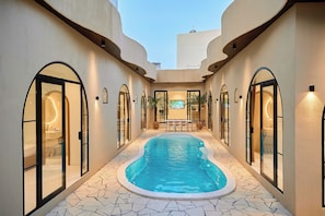 A swimming pool area with a tiled floor, arched doorways, and a seating area with a table and chairs. - Mediterranean pool villa near the beach (Thành phố Hồ Chí Minh)