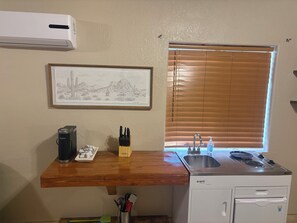 A compact kitchen with a built-in stove, a sink, and a window with blinds.