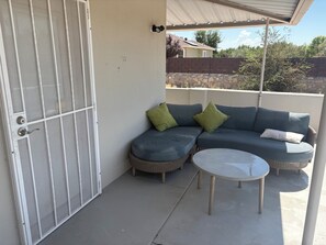 A covered balcony with a screened door, a blue sofa with green cushions, and a round table. - Cozy Parkside Studio, Full Kitchen, Queen Bed, Patio & Laundry (Las Cruces)