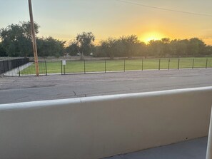 A view of a parking lot with a fence, a grassy area, and trees in the background.
