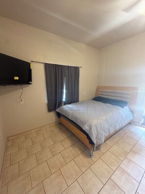 A bedroom with a bed, a television mounted on the wall, and a window with curtains. - Cozy Parkside Studio, Full Kitchen, Queen Bed, Patio & Laundry (Las Cruces)