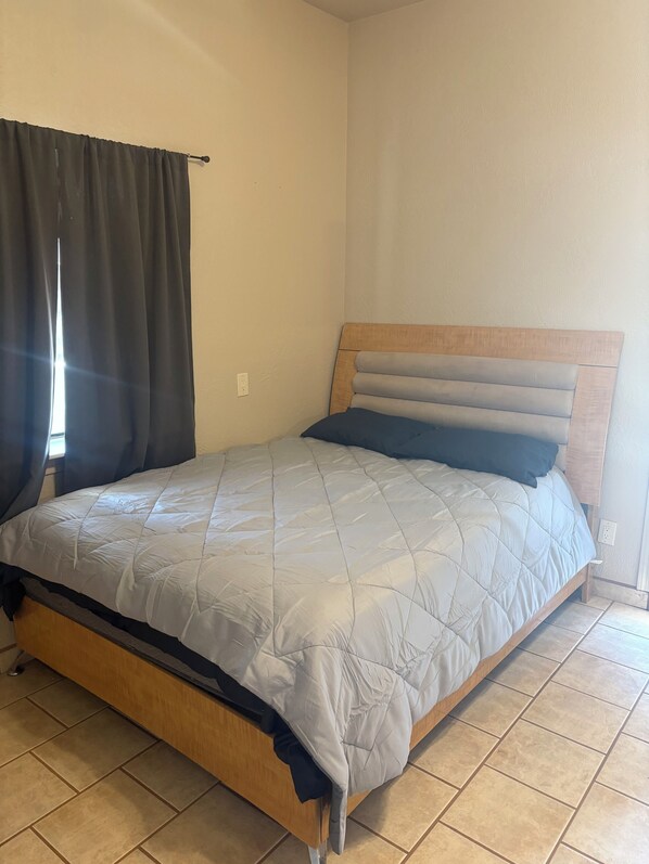 A single bed with a wooden headboard and a grey quilted bedspread.