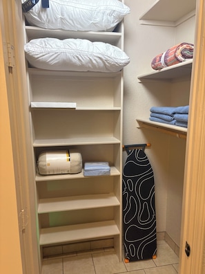 A closet with shelves containing folded towels, a rolled-up towel, and a black and white patterned item. - Cozy Parkside Studio, Full Kitchen, Queen Bed, Patio & Laundry (Las Cruces)