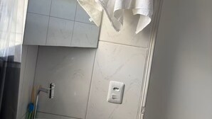 A bathroom with a white sink, a towel hanging on the wall, and a light fixture above the mirror. - Estúdio 4 - Vila Granados em Embu das Artes (Embu das Artes)