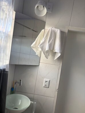 Een badkamer met een witte wastafel, een handdoek aan de muur en een lamp boven de spiegel.