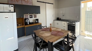 A modern kitchen with a dining area, featuring a refrigerator, stove, and a coffee maker. - Estúdio 4 - Vila Granados em Embu das Artes (Embu das Artes)