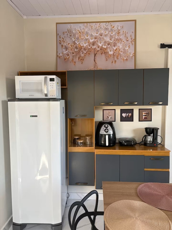 A compact kitchenette with a white refrigerator, a microwave, a coffee maker, and a kettle on the counter.