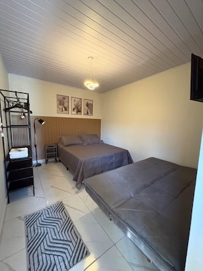 Een kamer met twee bedden, een hanglamp, een tv aan de muur en een ingelijst schilderij.