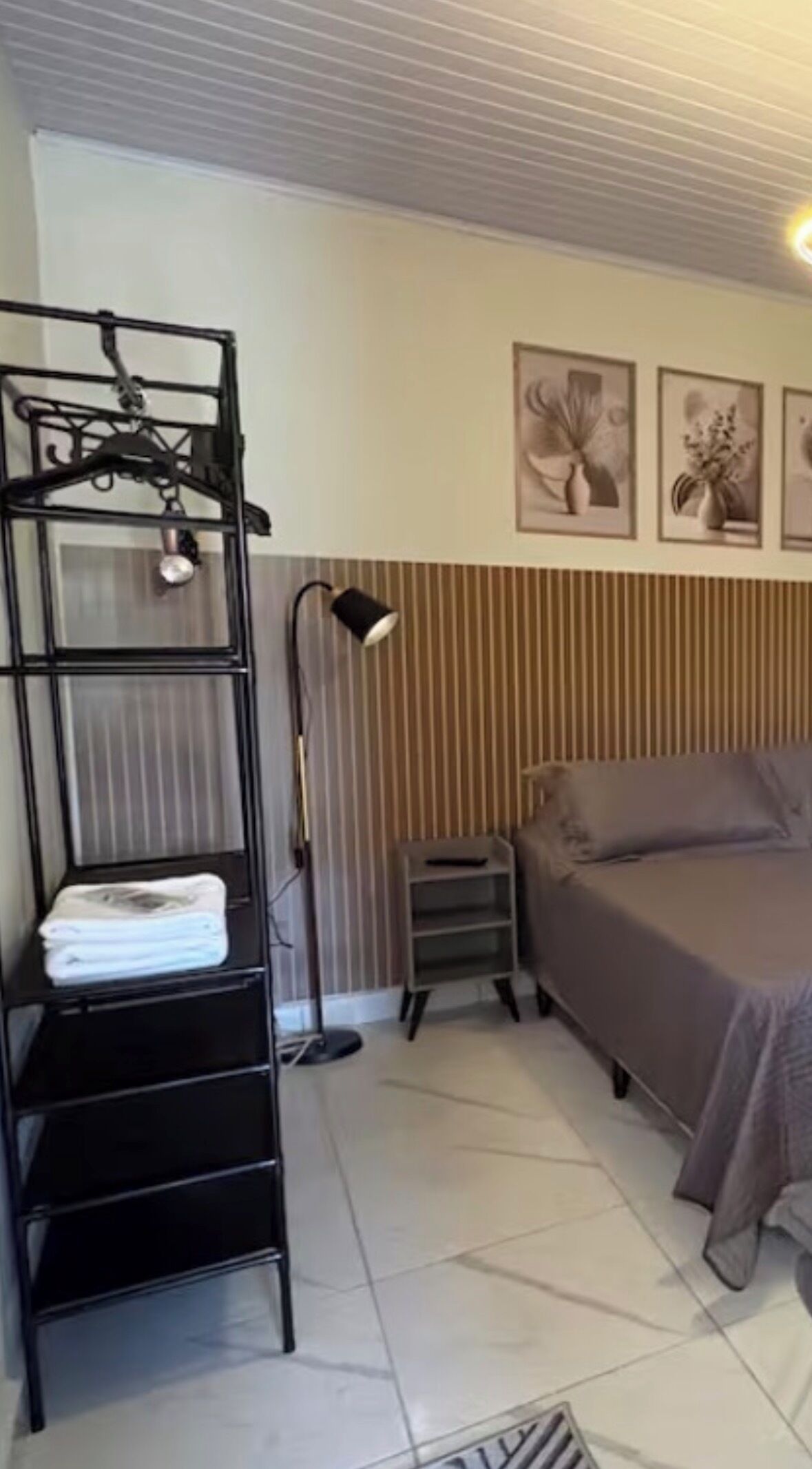 A bedroom with a bunk bed, a bedside table, a lamp, and a wall-mounted shelf with folded towels.