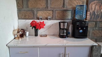 Une cuisine dotée d’un plan de travail en marbre, d’une machine à café, d’un distributeur d’eau et d’un vase rempli de fleurs rouges.