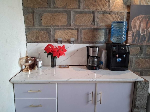 Una cocina con encimera de mármol, cafetera, dispensador de agua y un florero con flores rojas.