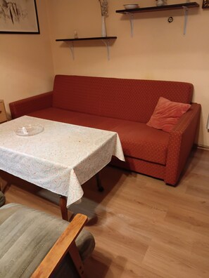 Ein Wohnzimmer mit einem roten Sofa, einem kleinen Tisch mit gemustertem Tischläufer und einem Holzstuhl.