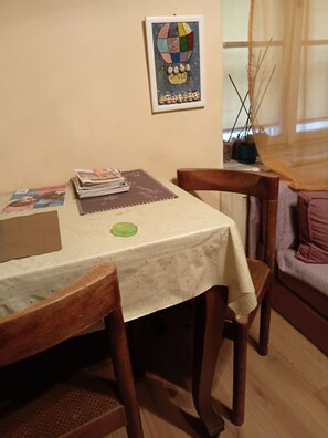 Ein Essbereich mit einem Tisch, der mit einer weißen Tischdecke bedeckt ist und von Holzsesseln umgeben wird. Über dem Tisch hängt ein gerahmtes Kunstwerk an der Wand.