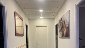 Un pasillo con una puerta al final, un espejo enmarcado a la izquierda y un cuadro a la derecha.