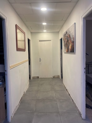 A hallway with a door at the end, a framed mirror on the left, and a painting on the right.