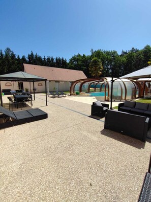 An outdoor patio area with a pool, covered seating, and a building in the background.