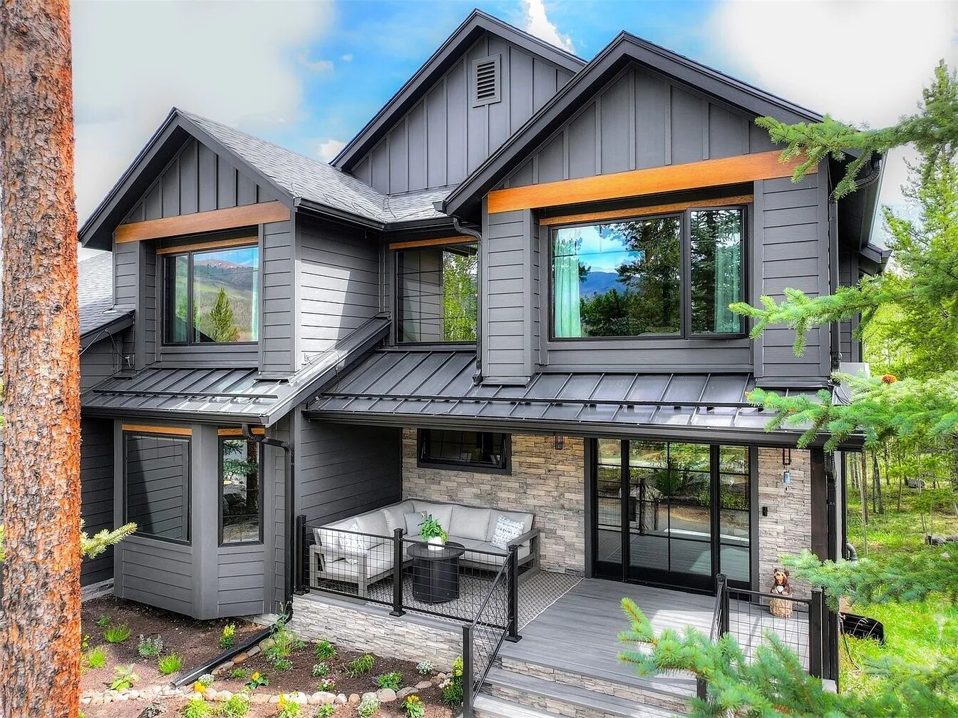 A modern two-story house with a covered patio, large windows, and a stone facade.