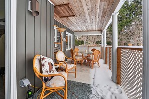 A covered outdoor seating area with wicker furniture and a glass table, surrounded by a wooden deck and a white lattice fence.