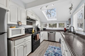 A modern kitchen with white cabinetry, stainless steel appliances, and a skylight.