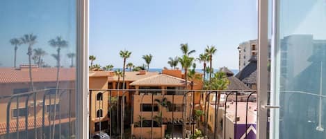 A view from a balcony with a clear sky, palm trees, and buildings with red-tiled roofs.
