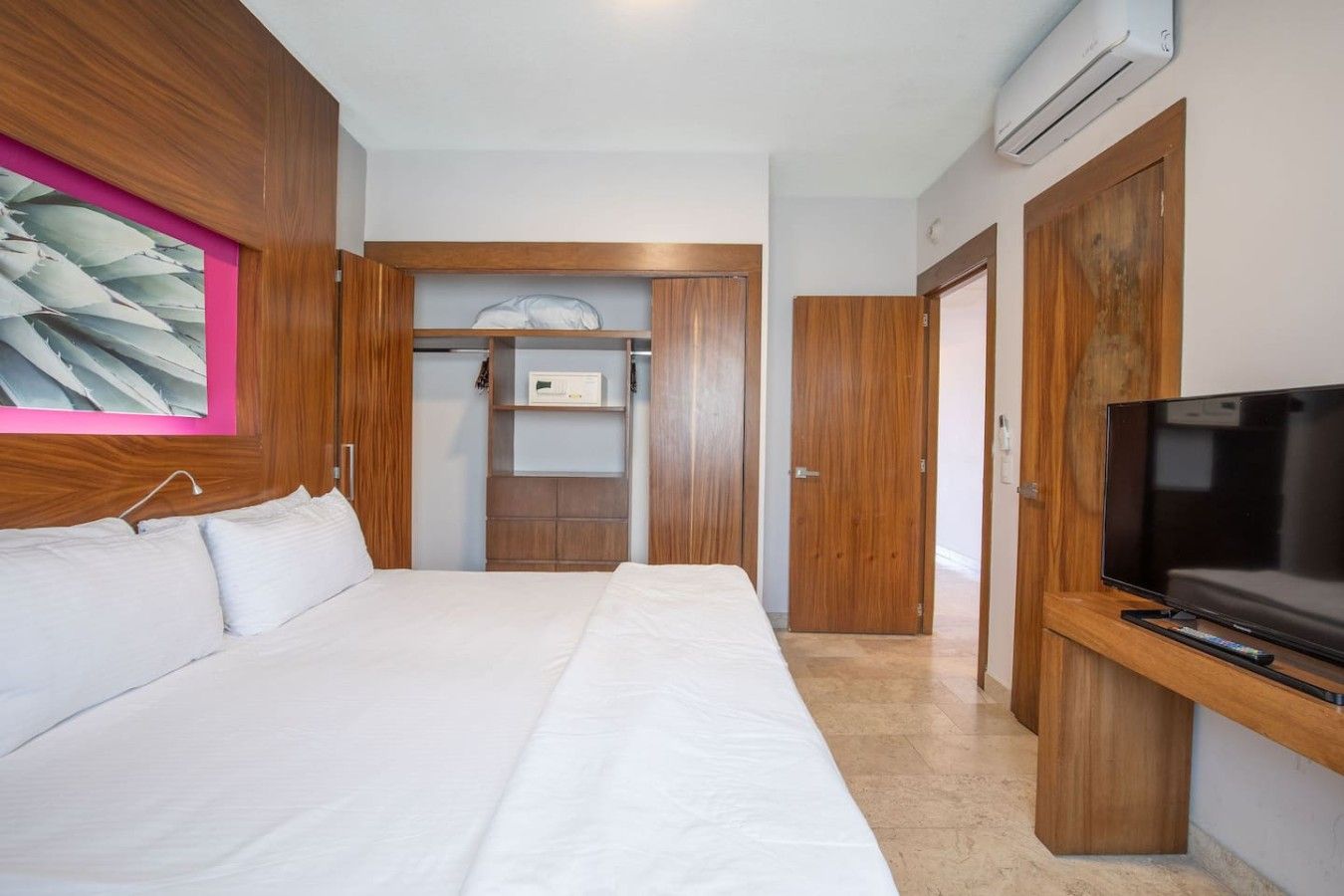 A hotel room with a bed, a television, a wardrobe, and a painting on the wall.