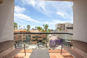 A balcony with a glass barrier, two chairs, a small table, and a view of palm trees and buildings. - Depto. a 5 min del mar y el centro de San Jose 106 (San José del Cabo)