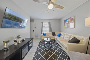 A modern living room with a sofa, a coffee table, a TV, and a ceiling fan.