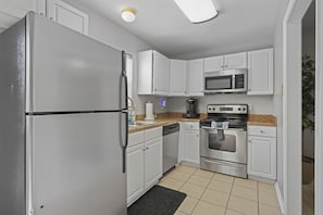 A compact kitchen with white cabinets, a stainless steel refrigerator, a microwave, a stove, and a dishwasher.