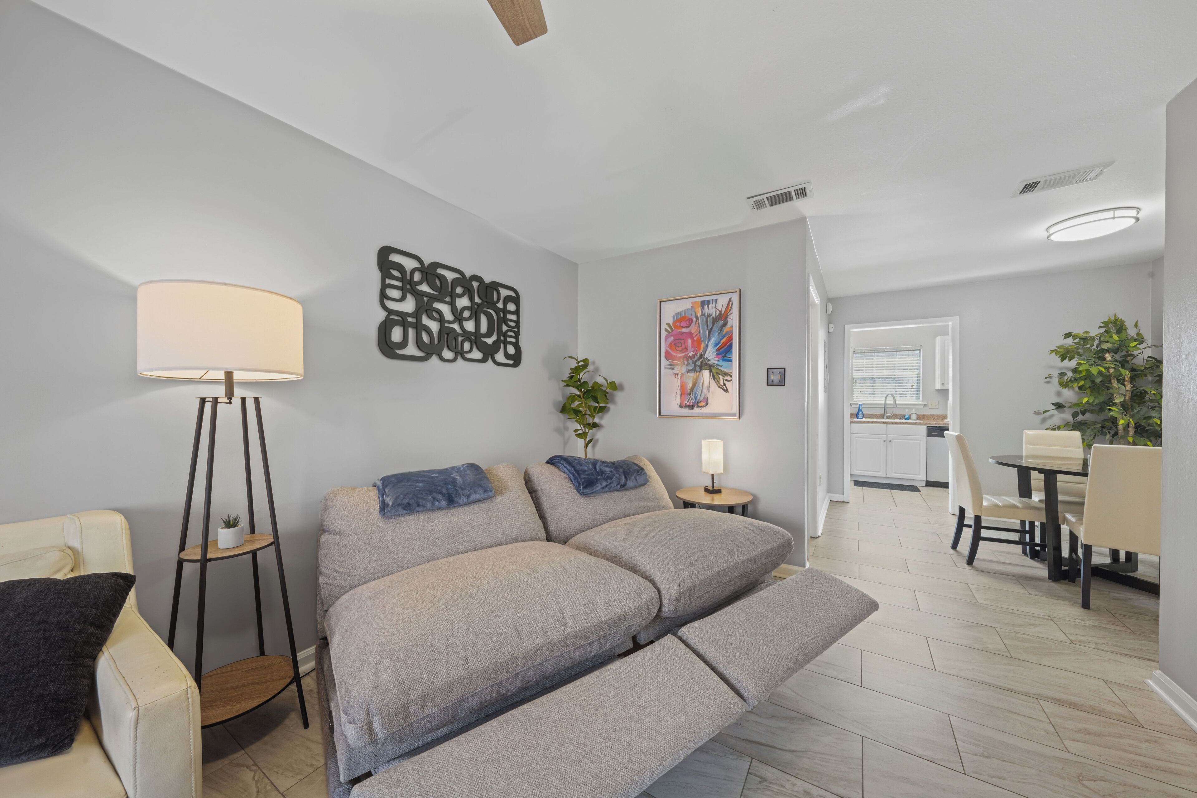 Un salon moderne comprenant un canapé, une lampe sur pied, un élément décoratif mural et un coin repas avec une table et des chaises.