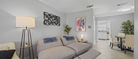 Un salon moderne comprenant un canapé, une lampe sur pied, un élément décoratif mural et un coin repas avec une table et des chaises.