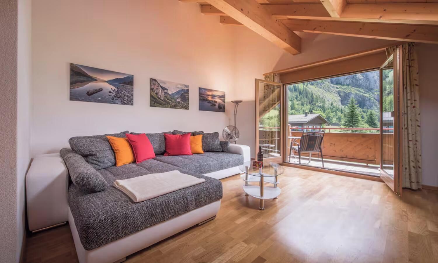 A modern living room with a sofa, a glass coffee table, and a view of a balcony with a wooden deck.